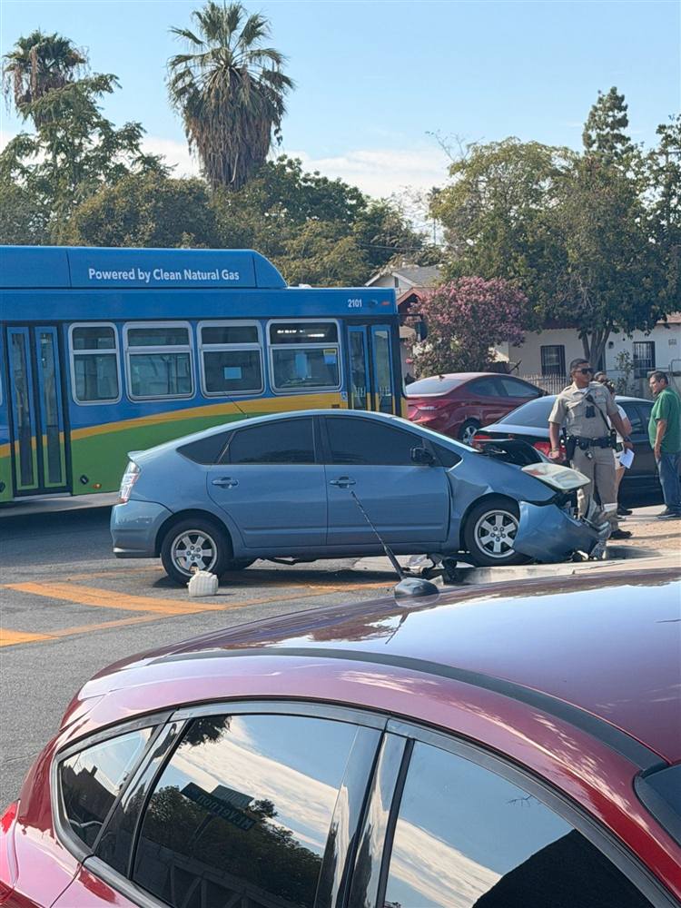 Damaged blue car at an intersection with an officer on scene